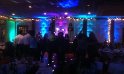 Here we programmed the lights to chase around the room for a cool effect. People dance on a dimly lit dance floor at an indoor event, surrounded by decorated tables and colorful lights.